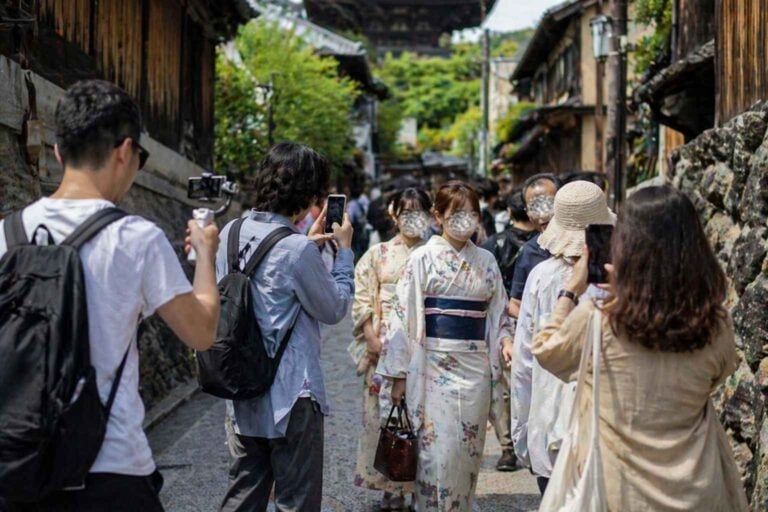 Tourists filming in a narrow Japanese street while pedestrians try to pass