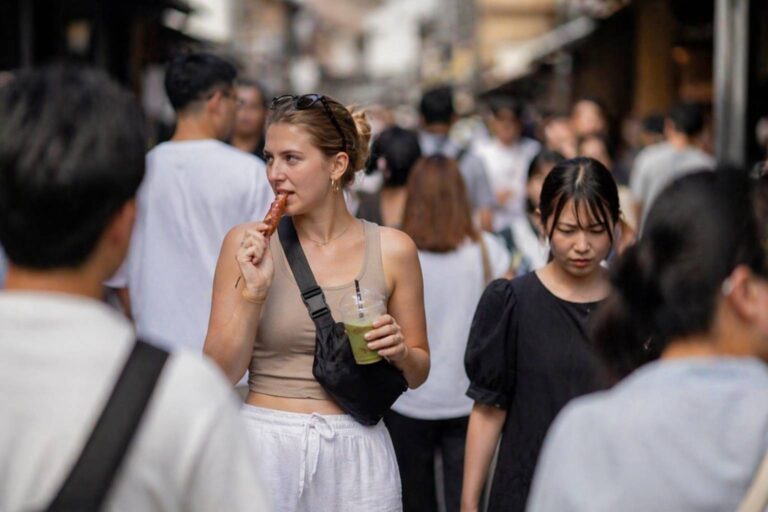 Traveler eating and holding a drink while walking through a busy street in Japan