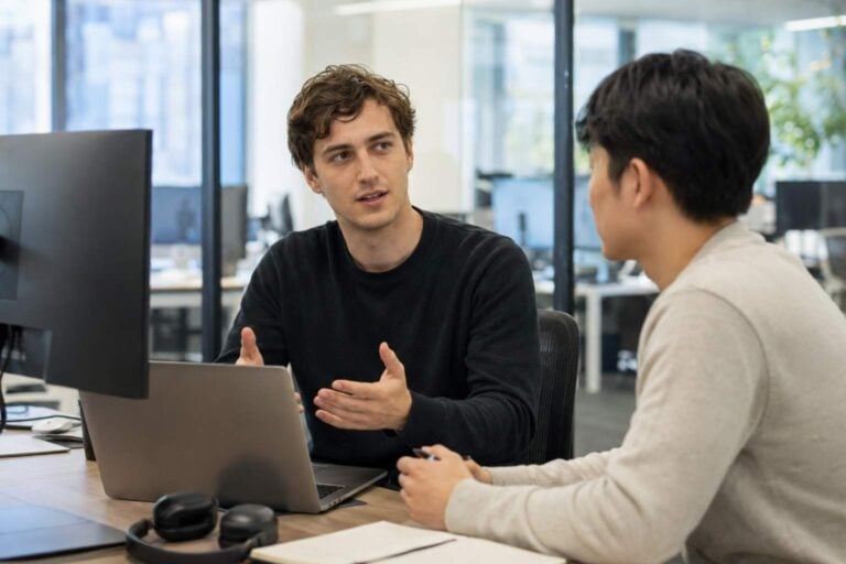 Foreign software engineer works at a laptop in a modern Tokyo tech office with a coworker nearby